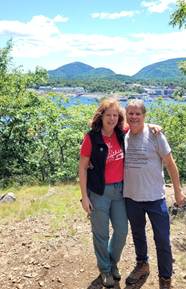 A person and person standing on a hill with trees and water in the background

AI-generated content may be incorrect.